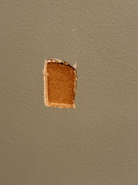 Närbild av en vägg med ett rektangulärt område där yttersta skiktet av färg och material är borta, vilket exponerar en djupare yta.