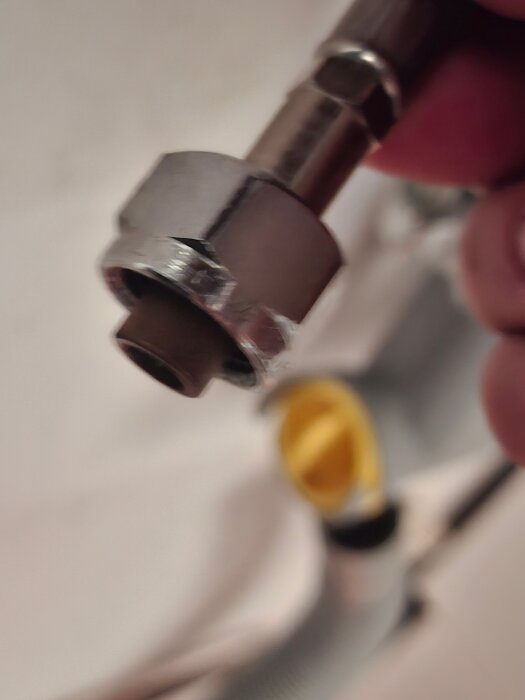 Närbild av en metallisk rörkoppling, troligen en del av ett VVS-system, med en mutter och ansluten flerviktsrör.