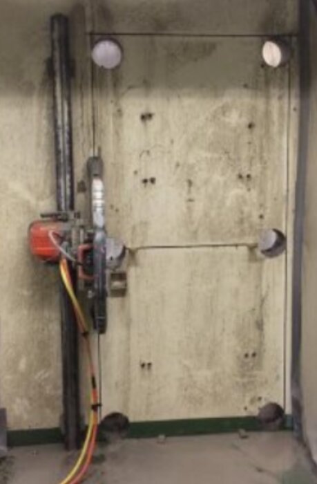 Betongvägg med verktyg för betongsågning monterat, redo för att kapa bort delen av väggen som angetts med borrade cirkulära hål.