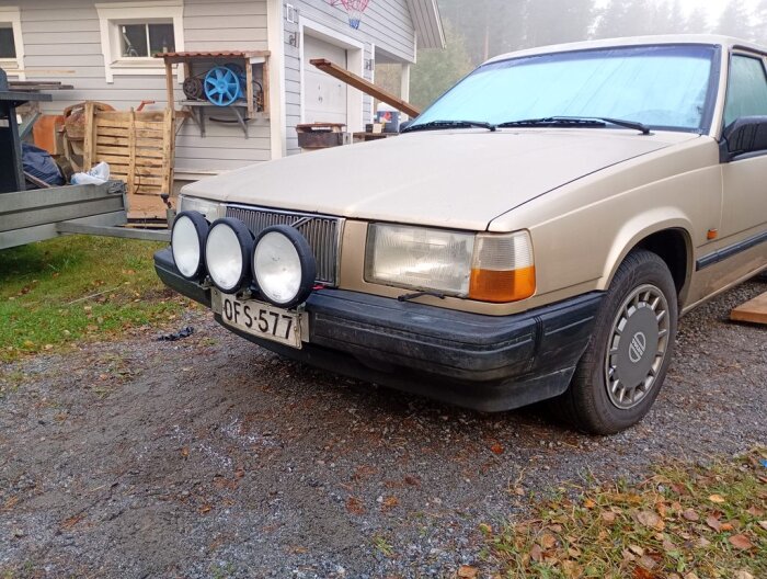 Beige Volvo 745 med tre extraljus monterade på fronten, parkerad framför ett hus.