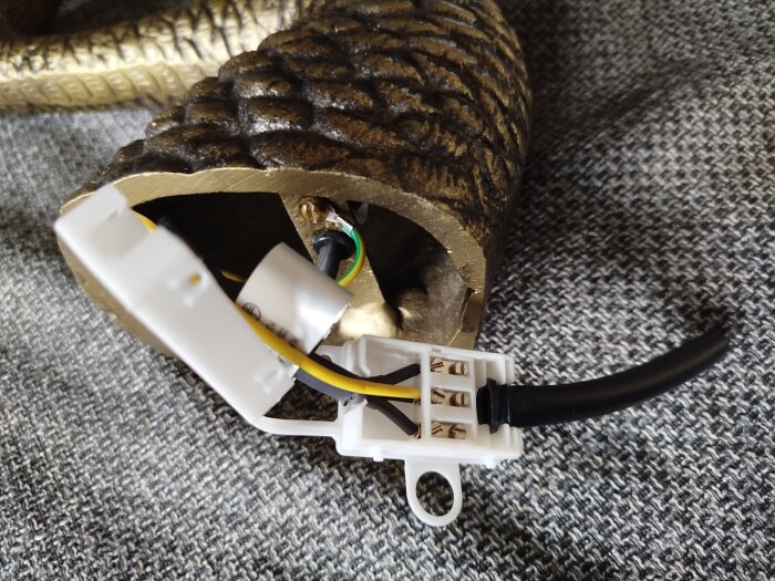 Elektrisk anslutning med kablar och en blänkande metalliskt föremål på en grå textilyta.