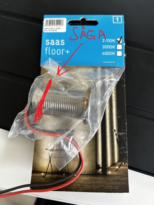 Förpackning med led-belysning, märkt "saas floor+", med tre avbockade färgtemperaturer. Handskriven anvisning "SÅGA" och pil pekar mot belysningen.