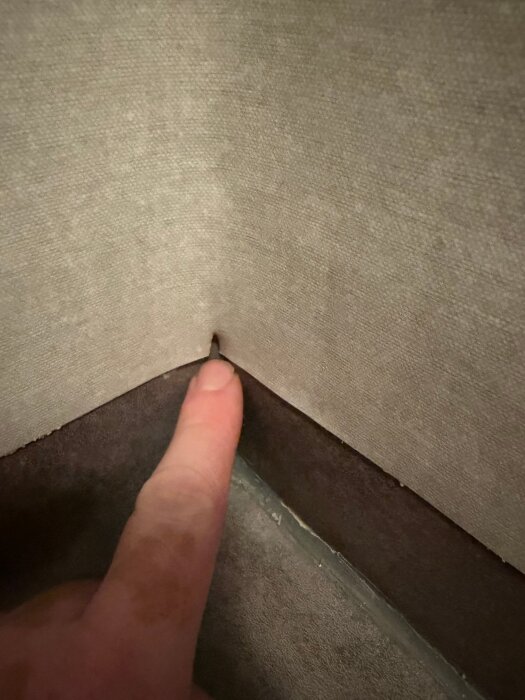 Våtrumsmatta med en glipa i hörnet där en fingerpekning visar en spricka mellan matta och vägg.