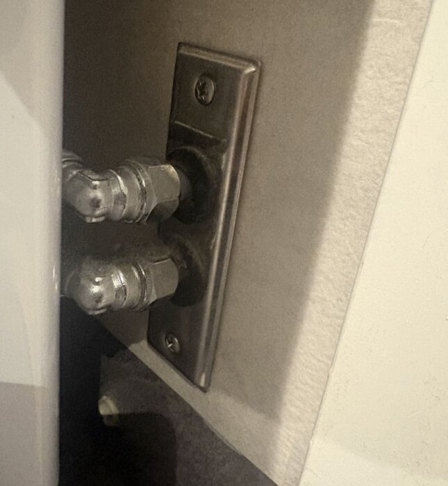 Vattenanslutning med två rör kopplade till en väggdosa bakom en tvättmaskin, inklusive en klämringskoppling och vinkelkoppling i metall.