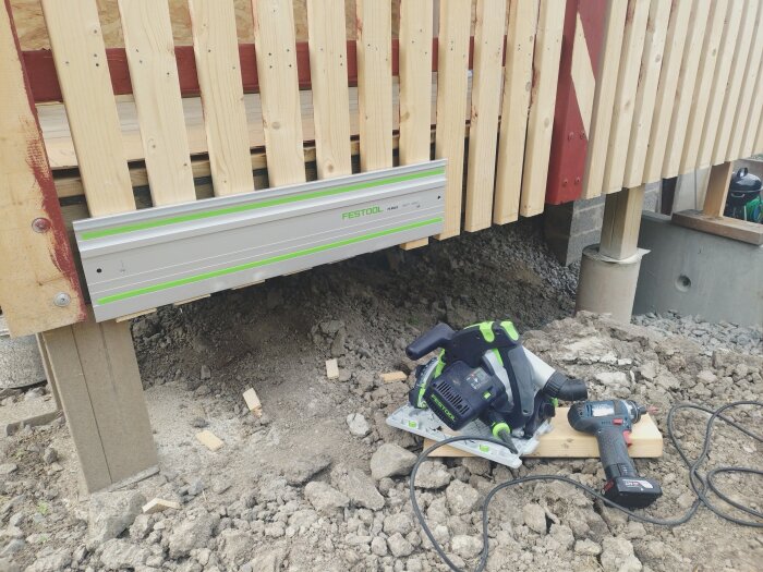 Cirkelsågskenor och verktyg på marken vid trästaket under byggnation.