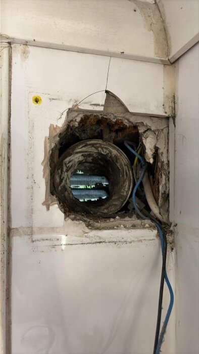 Ventilationshål i vägg med gammalt flexibelt rör och elkablar synliga. Kalkstensvägg med öppning förventilationsinstallation.