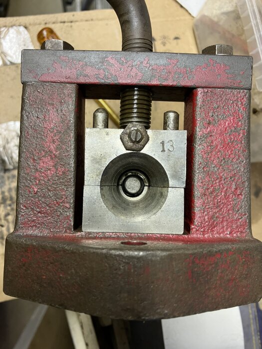 Rostig metallpress med röd färg och skruv, synlig arbetsyta, inställning för rörbearbetning, monterad på arbetsbord.