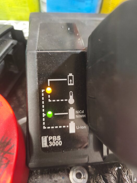 Laddare för PBS 3000 med orange och grön lampa tänd, visar laddningsstatus för Li-ion batteri.