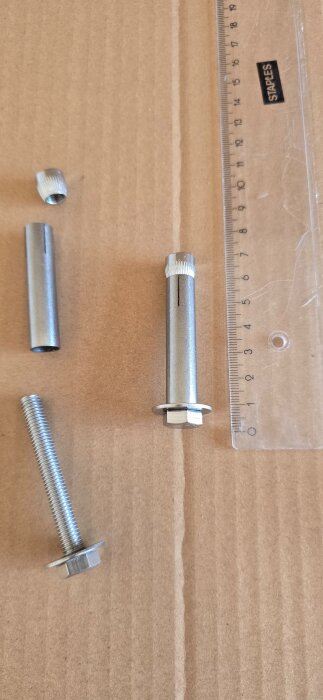 Metallkomponenter och en linjal på ett kartongunderlag, möjligen för infästning i tak.