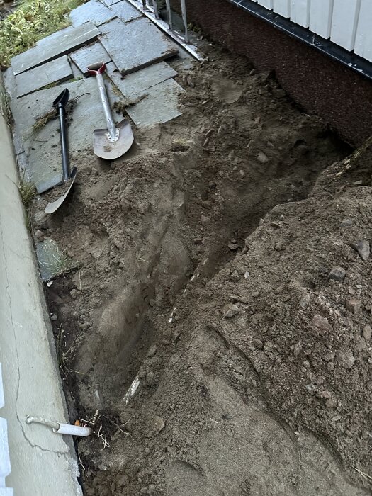 Markarbete vid hus där kablar dragits i markrör; två spadar syns vid sidan av en grävd fåra.
