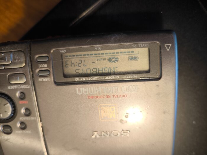 Sony mini-disc-spelare med LCD-skärm som visar text och batterisymbol. Knappar för funktioner syns på sidan av enheten.