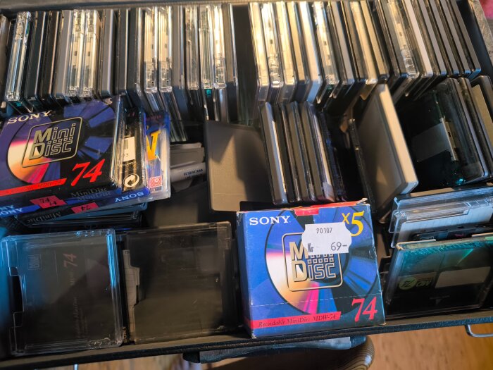 En samling MiniDisc-skivor i olika fodral, med några märken som Sony synliga, och en förpackning med fem skivor märkt "MiniDisc 74".