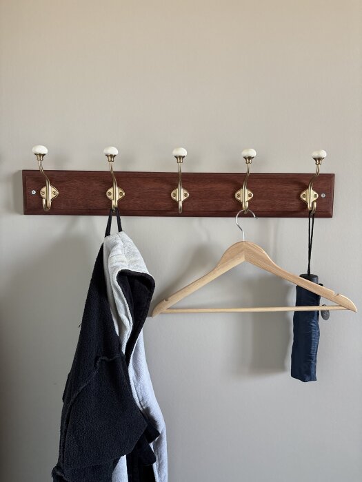 Vägghängare i mahogany med sex krokar, kläder och en galge hänger på krokarna.