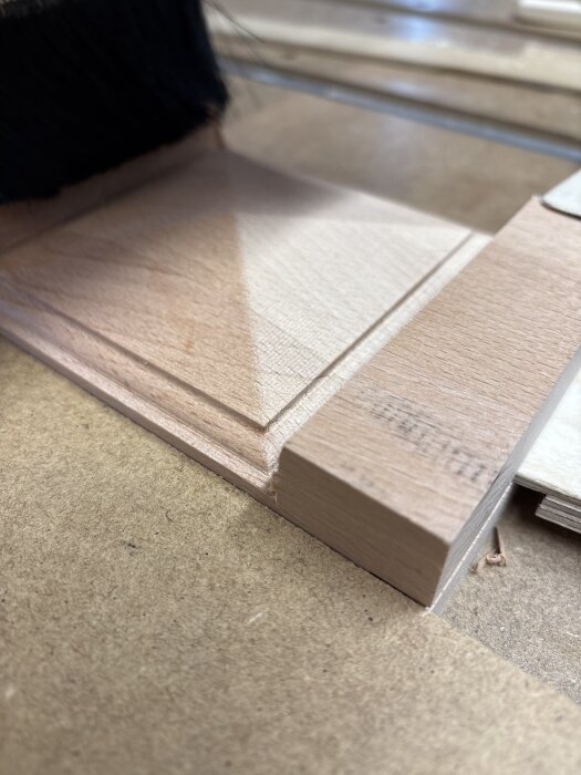 Träskiva med detaljerad fräsning skapad med CNC-maskin, nära en svart borste på arbetsbänk.