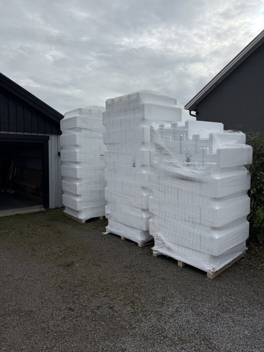 Fyra pallar med poolmaterial, inslagna i plast, står utanför ett garage på en grusuppfart under en molnig himmel.