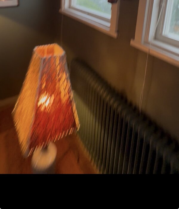 Suddig bild av ett element och en bordslampa med färgglad skärm framför ett fönster.