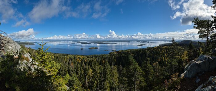 Utsikt över ett skogslandskap med sjöar och öar under en blå himmel med moln.