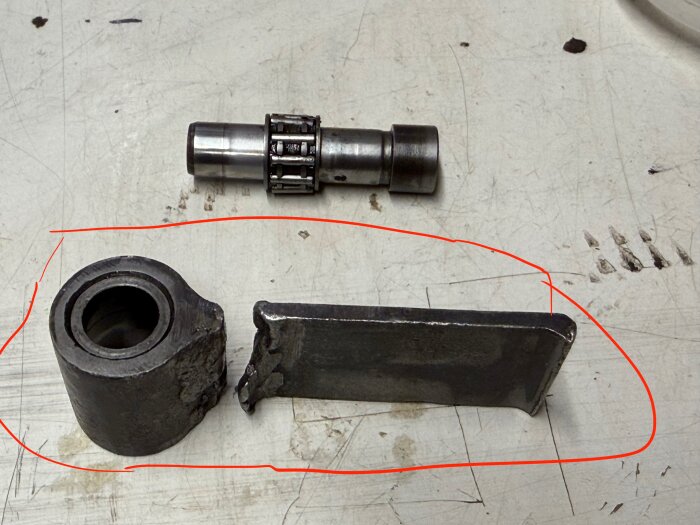 Verktygsdelar på arbetsbänk, en cylinder och en rektangulär metallbit, markerade med röd linje, sannolikt relaterade till borrprojekt.
