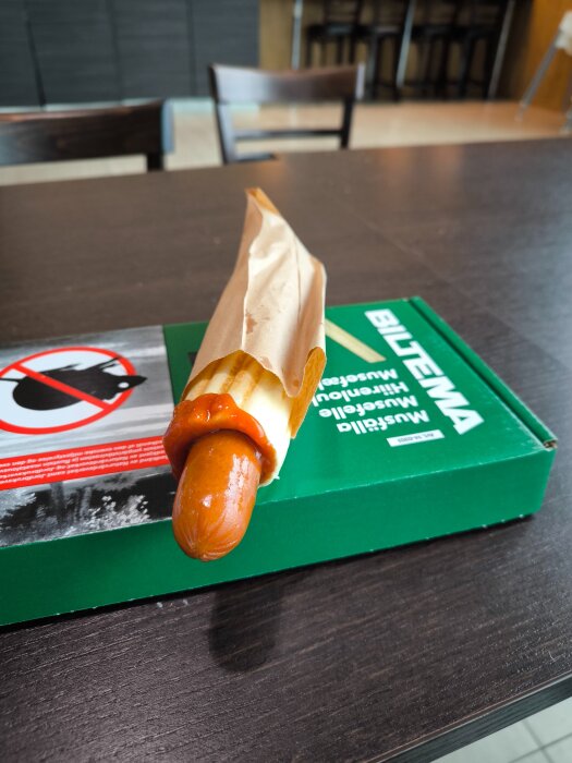 En korv med bröd och ketchup ligger på en Biltema-katalog på ett bord i vad som verkar vara en restaurangmiljö.