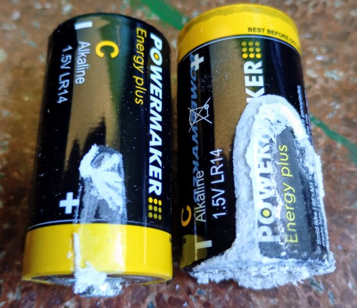 Två alkaliska C-batterier med läckage och frätande substans på ytan, en från Netto, ligger på ett bord.