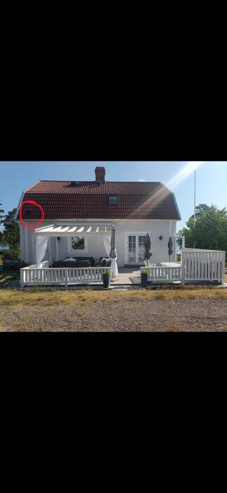 Fasaden på ett hus med rödtegeltak och altan. En avluftning är markerad med en röd cirkel nära taket.
