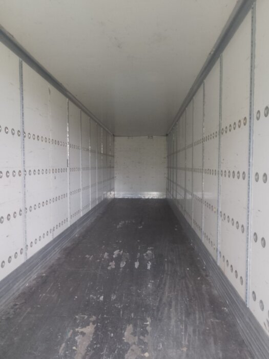 Interiör av en tom långsmal container med vita väggar och mörkt golv, visar utrymmet och takhöjden.