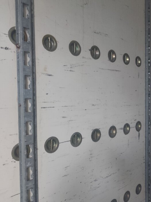 Vit betongvägg med rader av metallskruvar och stålram på sidan.