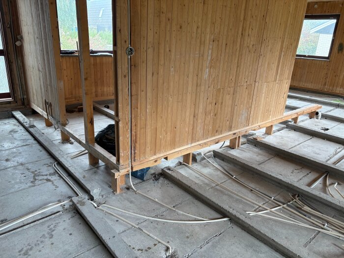 Rivna golv med mellanliggande träblock på betongbjälklag och innerväggar. Kablar och rör syns på betongytan.