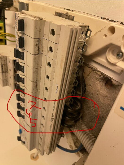 Elcentral med flera automatsäkringar, varav några är märkta med "5" och "7" i röd text. Kablar syns i det öppna utrymmet bakom.