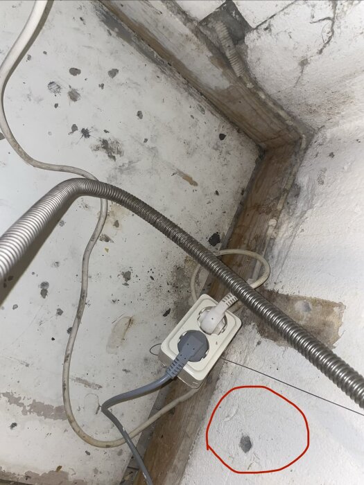 Vägguttag med kablar i ett hörn, shuko-uttag och hål i väggen markerat med en röd cirkel, möjligen för tidigare installation.