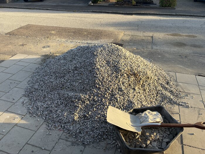 Hög av bergkross och makadam på trottoar, spade med trälåda vid sidan.