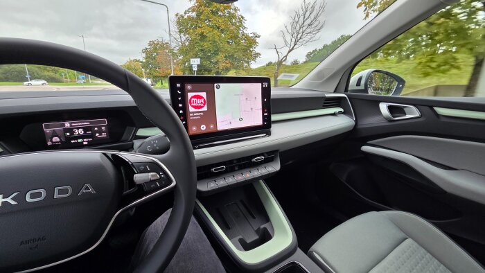 Instrumentpanelen i en Skoda elbil med Android Automotive, visar navigering och radiodisplay, fotograferad inifrån bilen med utsikt mot en rondell.