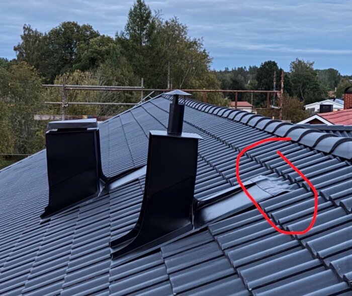 Tak med sneda och knögliga ventilationshuvar i svart plåt, omgiven av träd och byggnadsställningar, röd markering på ena delen av taket.