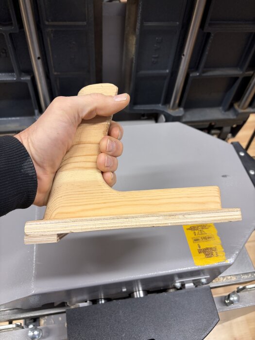 Hand håller en trähållare för tryckning av träobjekt på industriell maskinbakgrund.