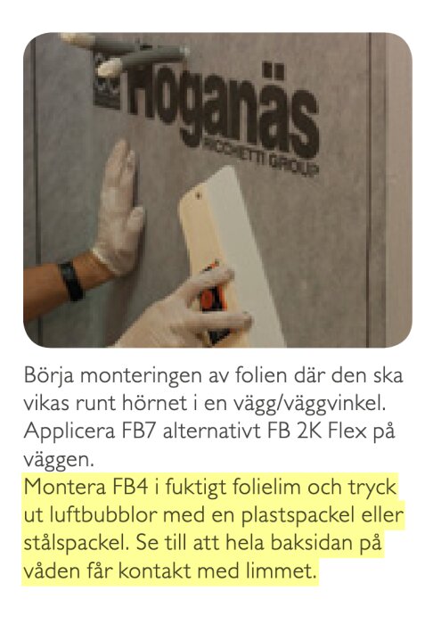 En person använder en spackel för att applicera folie på en vägg med texten "Höganäs" synlig.