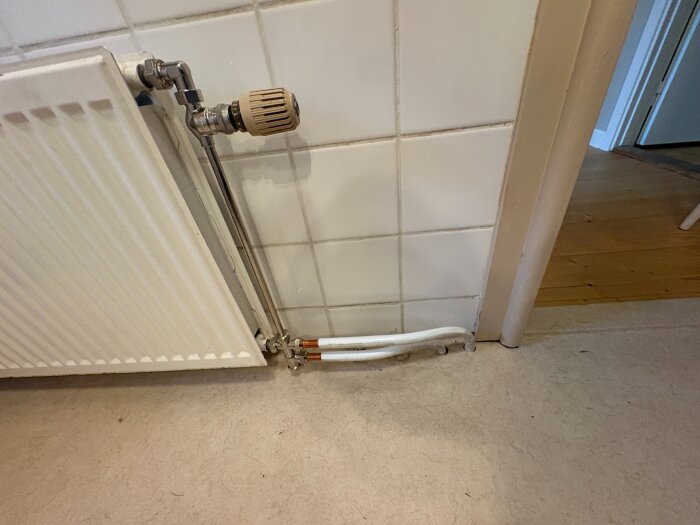 Radiator tillhörande ett värmesystem med kopparrör och avstängningsventil, monterat vid en kaklad vägg och parkettgolv.