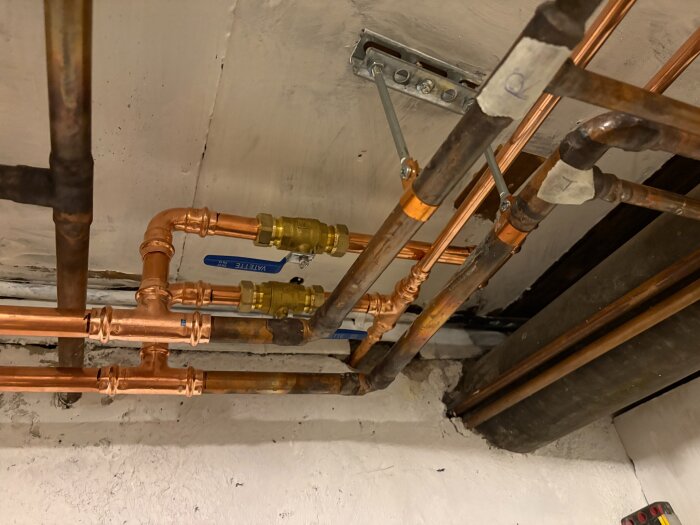 Koppar- och järnrör i källartak med avstängningsventiler, del av ny tvårörsslinga för elementrenovering.