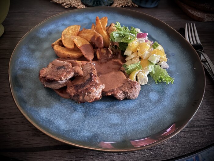 Stekt fläskfilé med pepparsås, serverad med klyftpotatis och sallad på en tallrik.
