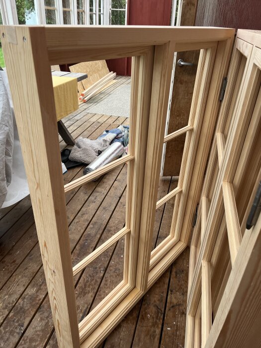 Nya träfönster med karmar stående på en veranda, redo för målning och glasning. Bakgrunden visar träplankor och en filt.