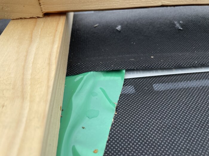 Takläggning med exponerad trästruktur, grön väv och svart papp, visar på detalj av bristfällig konstruktion efter påbörjad renovering.