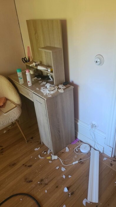 Krossade speglar och lampor på golvet vid ett sminkbord efter en olycka med en stege under takarbete.