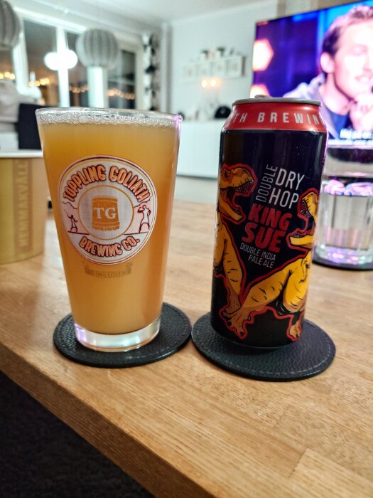 Ett glas fyllt med öl från Toppling Goliath bredvid en burk Double Dry Hop King Sue på ett bord.