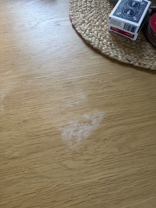 Fläckar på ett träbord efter att en rostad macka legat direkt på ytan, bredvid en flätad tablett och en kortlek.