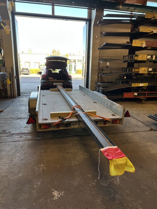 En IPE160 balk fastspänd på en släpvagn i ett garage, med en bil i bakgrunden och metallstänger på en hylla.