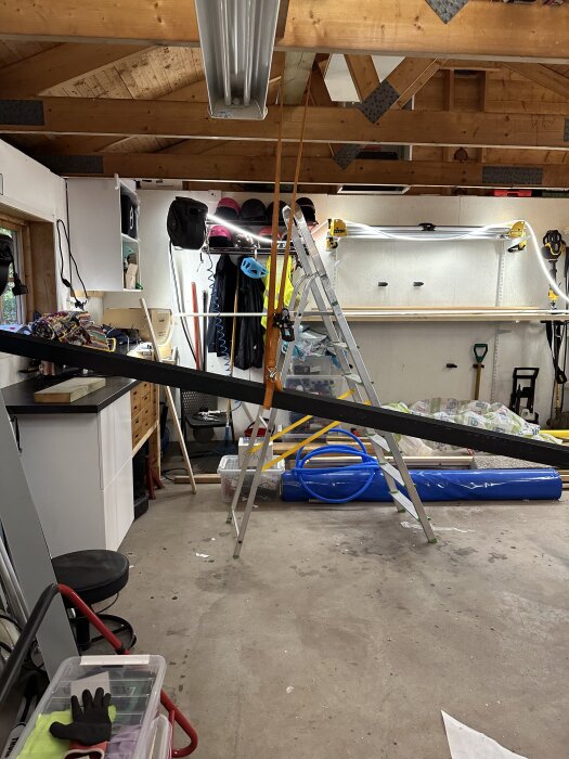 Garagetak med monterad IPE160 stålbalk, synliga träbalkar, arbetsbänk, stege och verktyg.