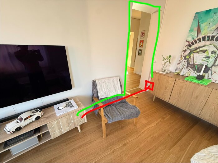 Vardagsrum med möbler, TV och konstverk. En grön linje markerar dörröppning, och en röd linje visar en möjlig kabeldragning längs golvet.