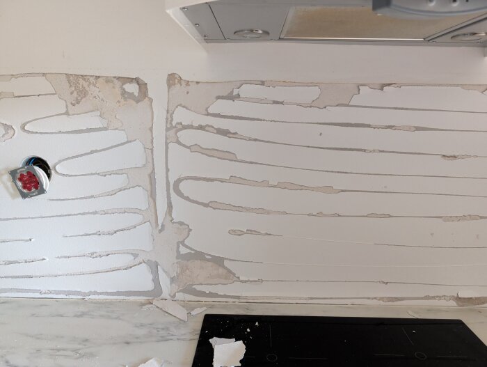 Vägg med borttagna kakelplattor i kök, redo för spackling och målning.
