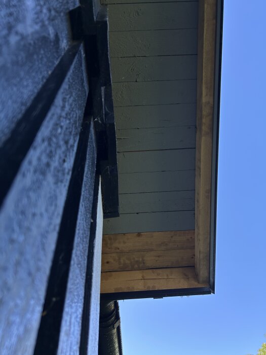Närbild av svartmålade träväggar och takfot på en byggnad under klarblå himmel.