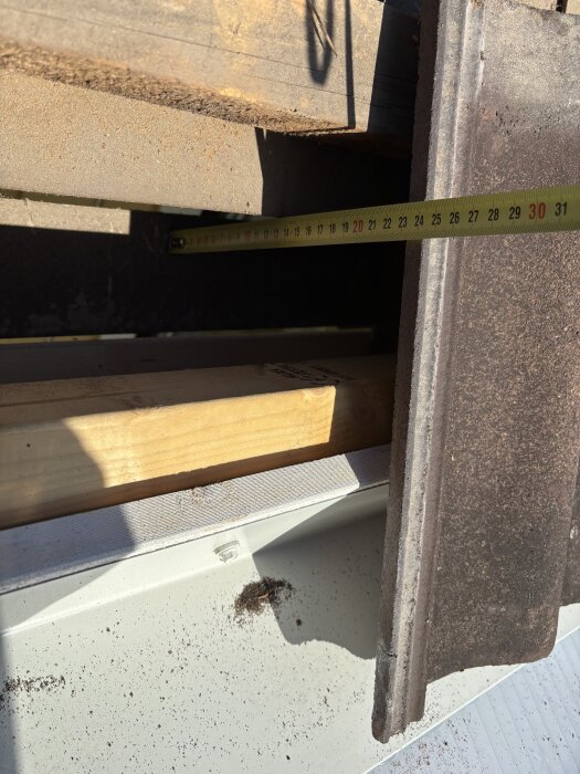 Inspektionshål i tak visar avstånd, med måttband på 120mm, mellan innertak och masonit. Träregel och plåt ses också i bilden.