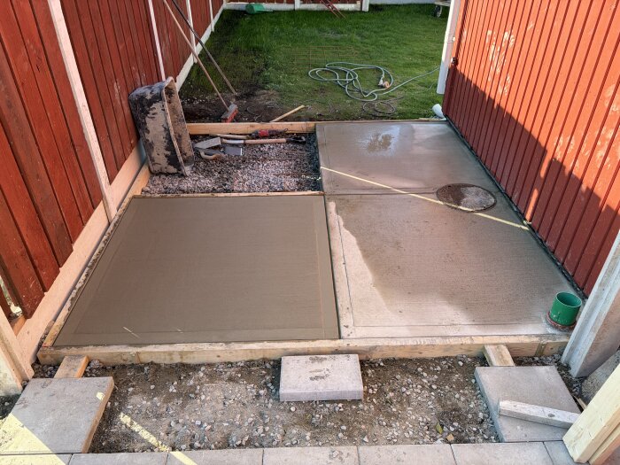 Betongplattor nygjutna mellan röda träväggar med verktyg och en hink i bakgrunden.